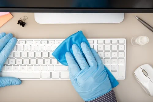 Gloved cleaner disinfecting an office keyboard and desk during a New Jersey commercial cleaning visit