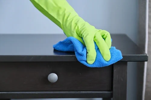 Gloved hand wiping dust from a dark wood dresser with a microfiber cloth during a whole-home deep cleaning