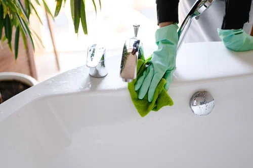 Cleaner in green gloves wiping a bathroom sink during a recurring home cleaning service in New Jersey