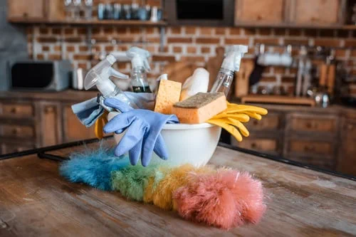 Professional house cleaning supplies with gloves and a duster on a wooden counter in a warm lived-in home kitchen